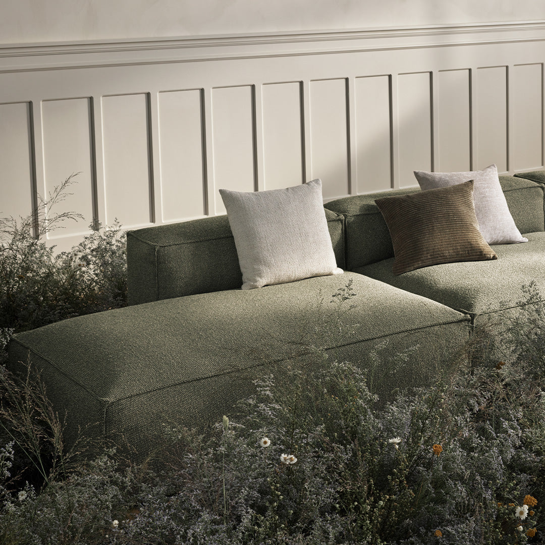 "Green fabric sofa with textured cushions in white, cream, and brown against a natural backdrop."