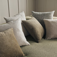 Assorted decorative pillows in muted tones of beige, gray, and earthy patterns on a soft green background.
