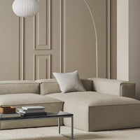 Beige sectional sofa with subtle texture, paired with a minimalist white pillow and sleek gray coffee table in a neutral setting.