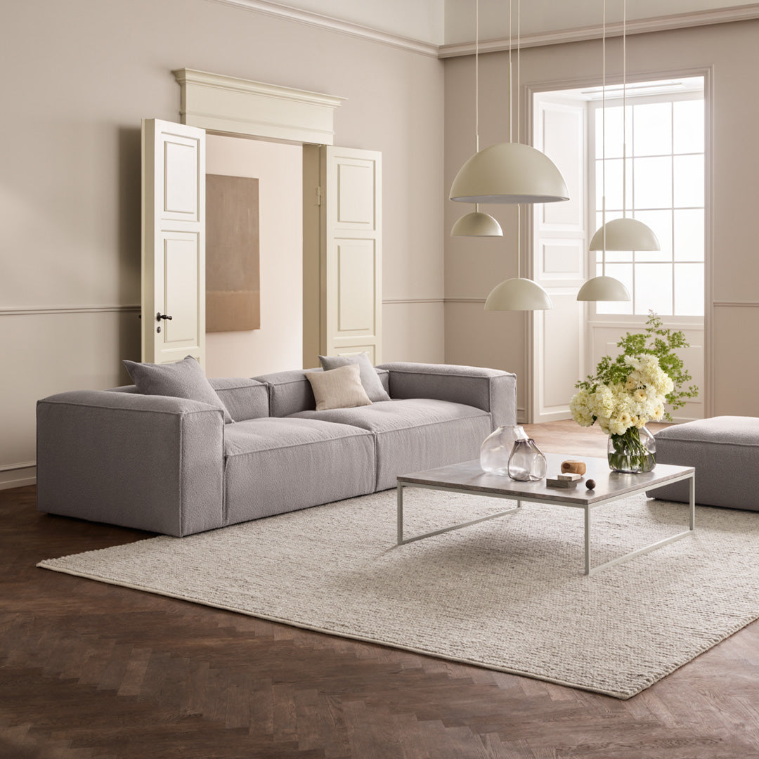 Sleek gray sofa on light-colored rug in a modern, neutral-toned room with soft white lighting.