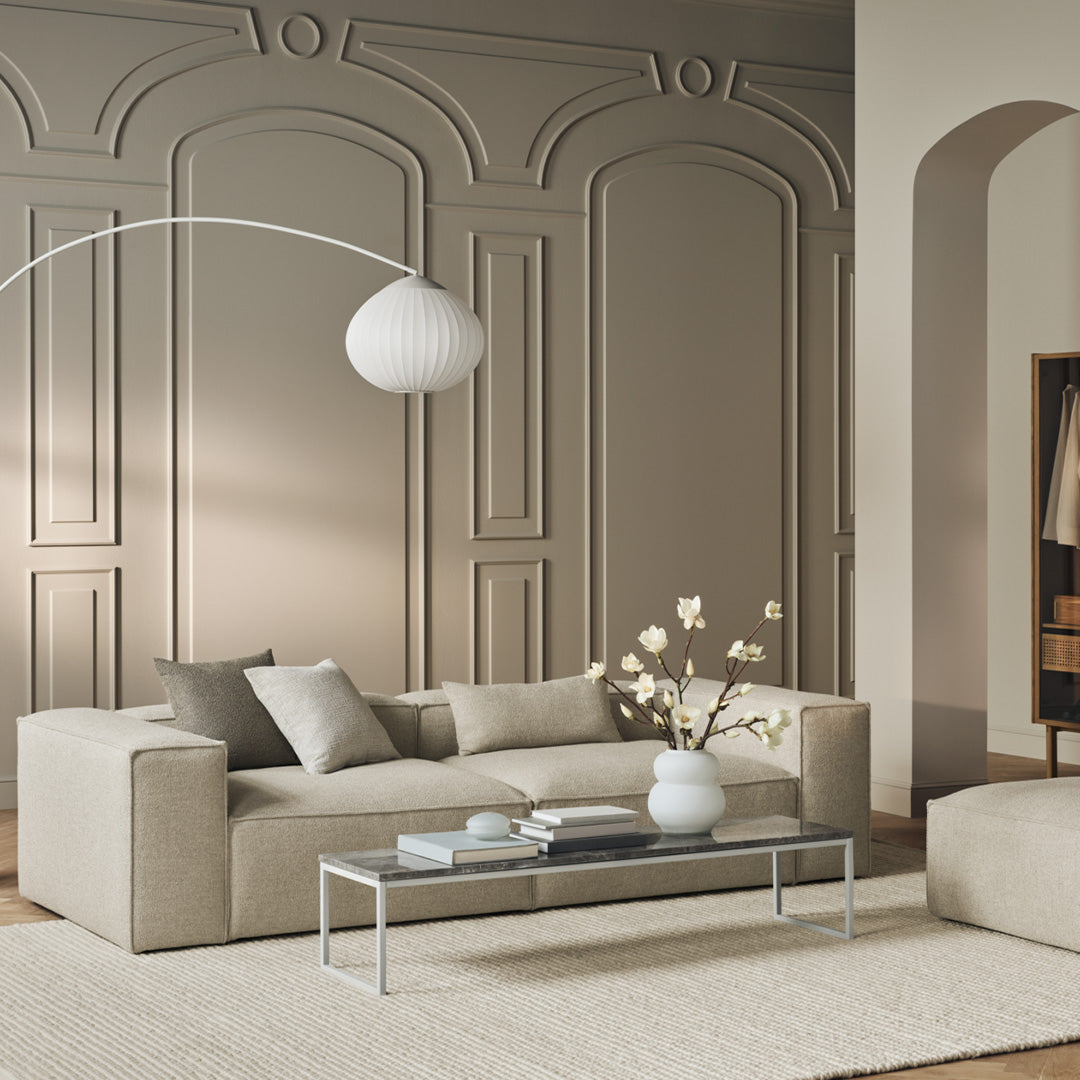 Beige sofa with light gray pillows and a white coffee table against a soft taupe wall and textured beige rug.