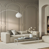 Beige sofa with light gray pillows and a white coffee table against a soft taupe wall and textured beige rug.
