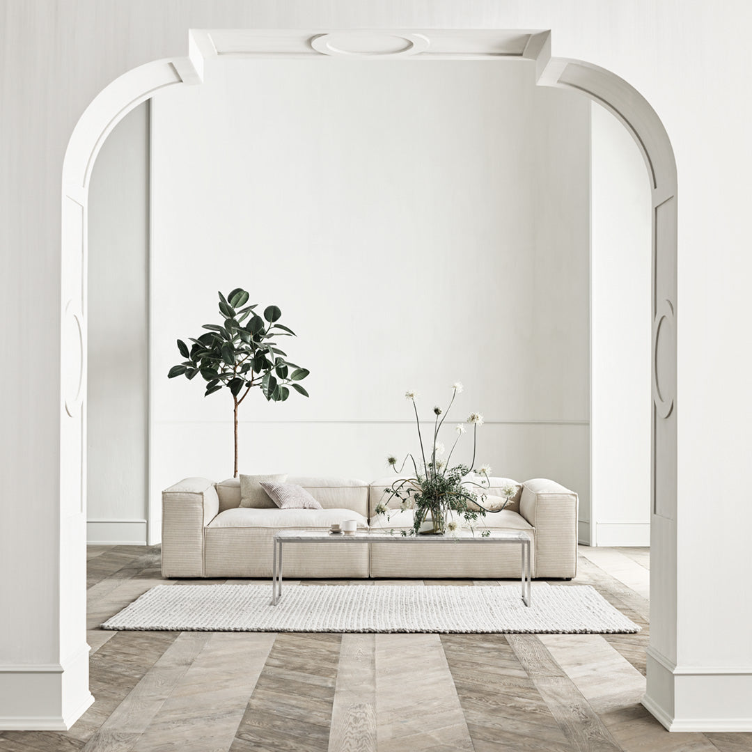 "Neutral beige sofa with white decorative elements, soft textures, and a light wood floor pattern."