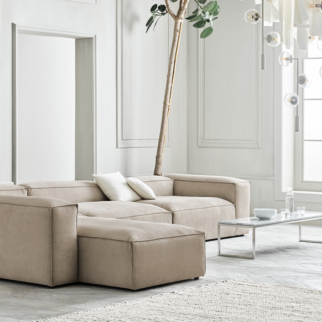 "Beige sectional sofa with clean lines and a modern fabric texture, complemented by a light gray rug and neutral decor."