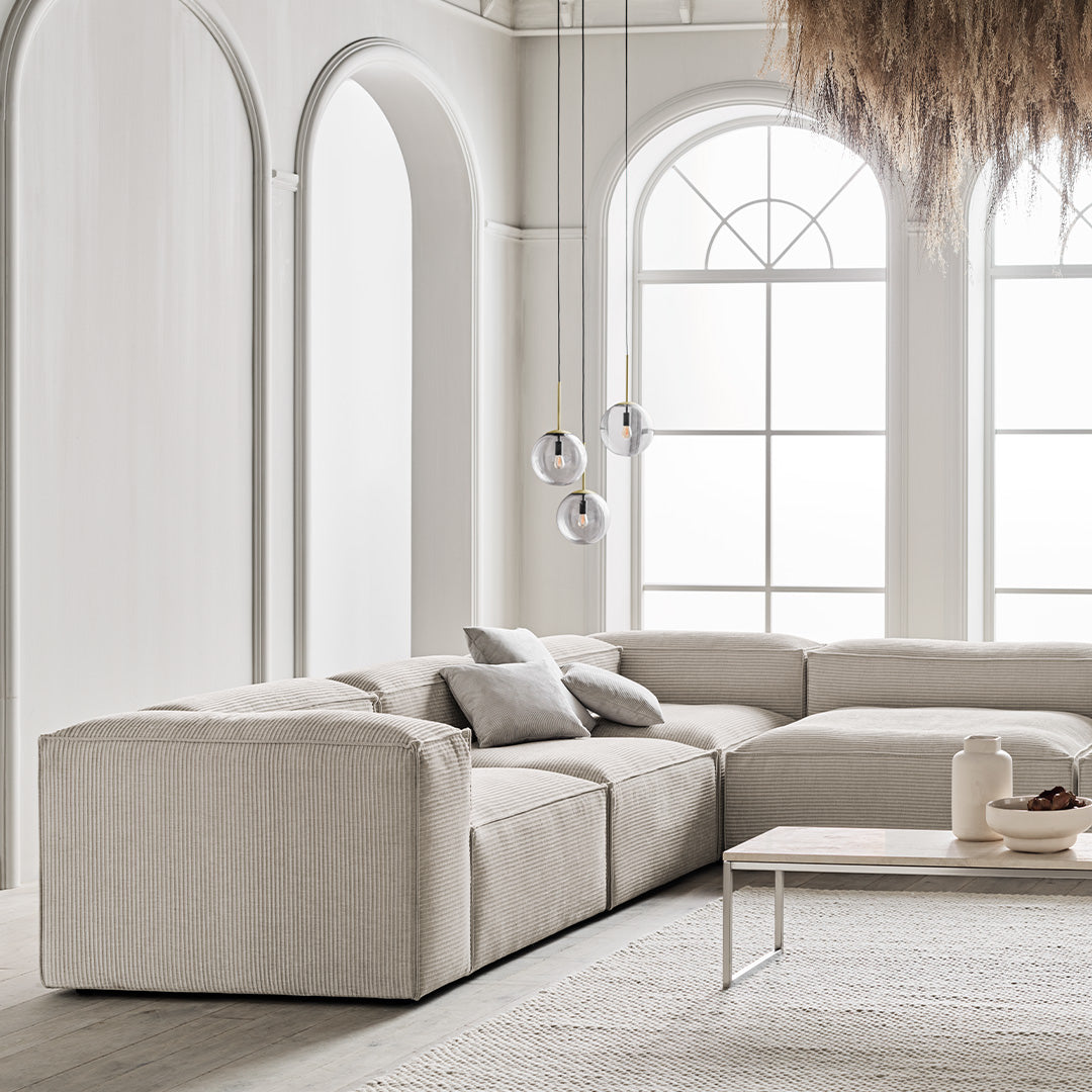 Beige sectional sofa with subtle texture, complemented by soft gray pillows in a minimalist, light-filled room.
