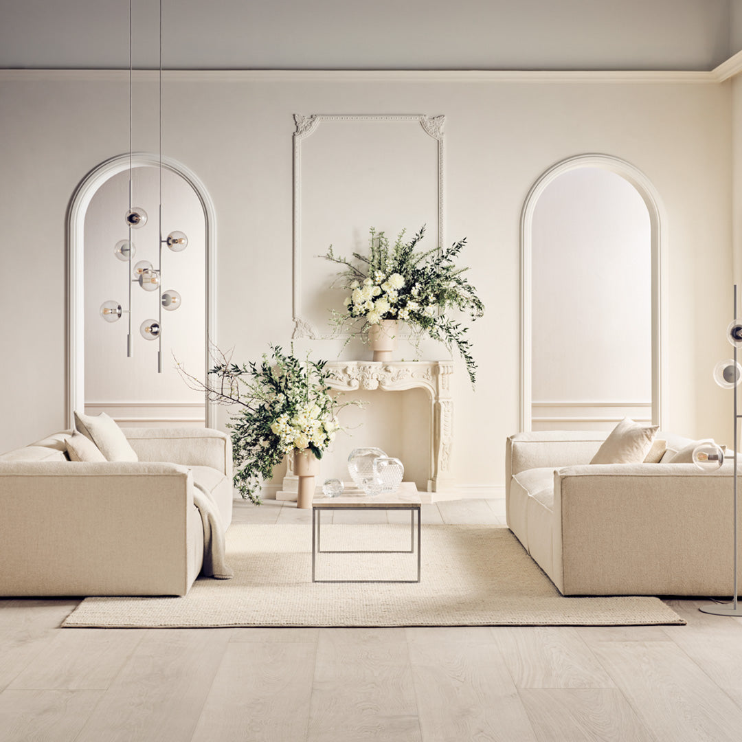 Elegant beige sofas with subtle textures, paired with soft white decor and lush green plants in a minimalistic setting.