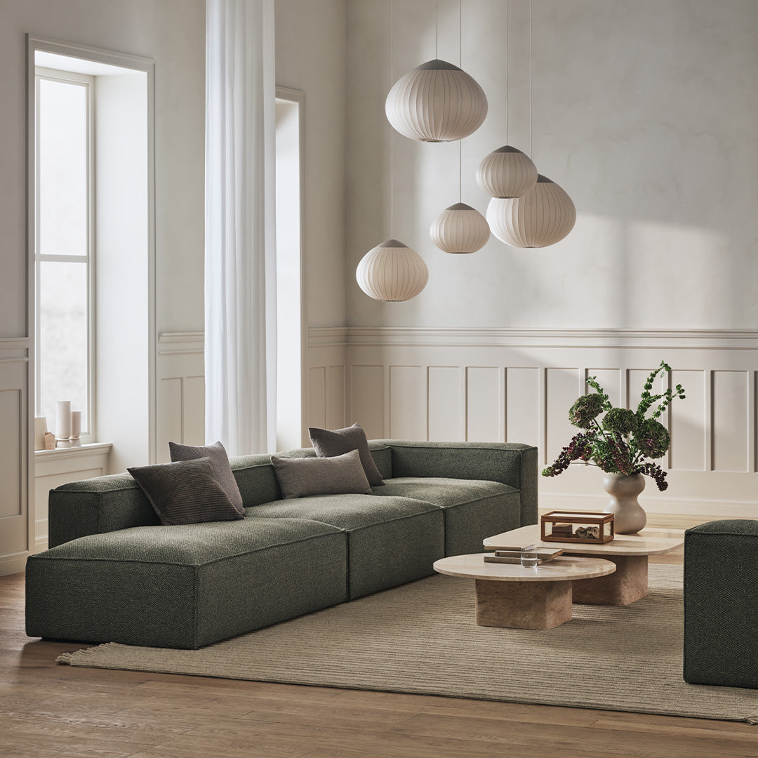 Modern green sofa with soft fabric, complemented by beige accents and light wooden furniture in a bright, minimalist setting.