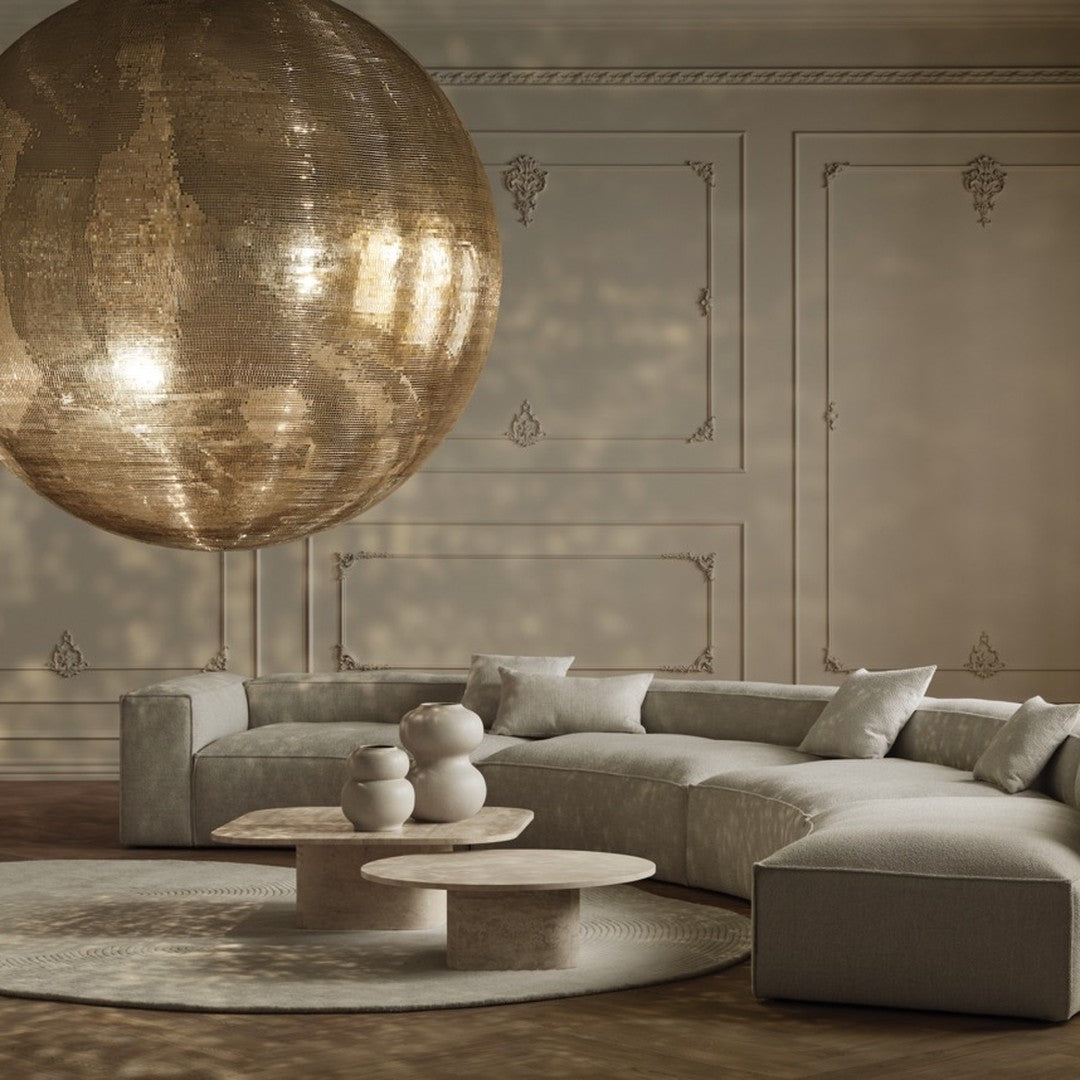 Light beige curved sofa with textured cushions, natural stone tables, and a shimmering gold pendant light.