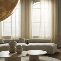 Soft beige sofa with textured cushions, light wooden table, and neutral-toned ceramic vases in a bright, airy room.