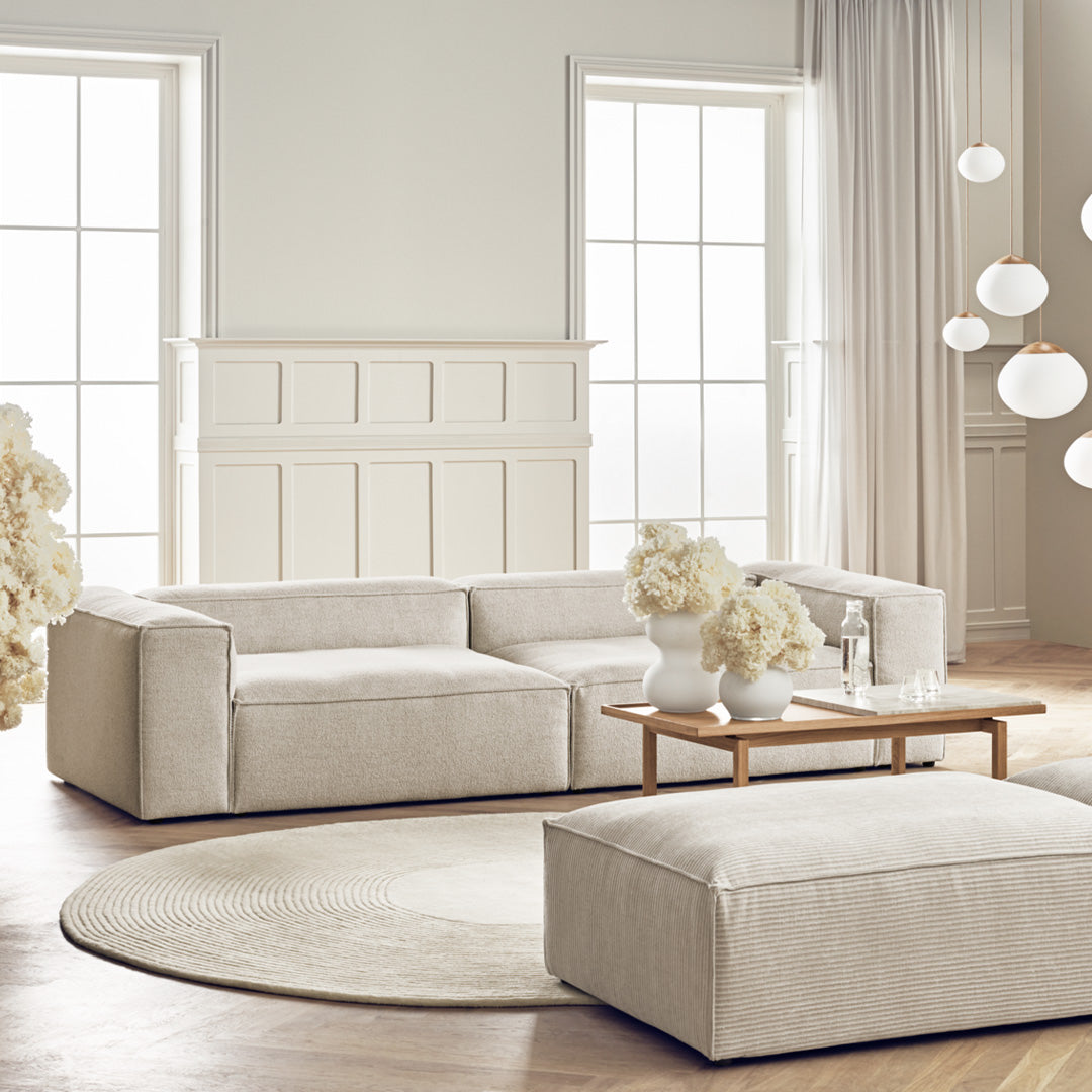 Light beige modular sofa with a soft texture, paired with a round cream rug and neutral decor in a bright, airy room.