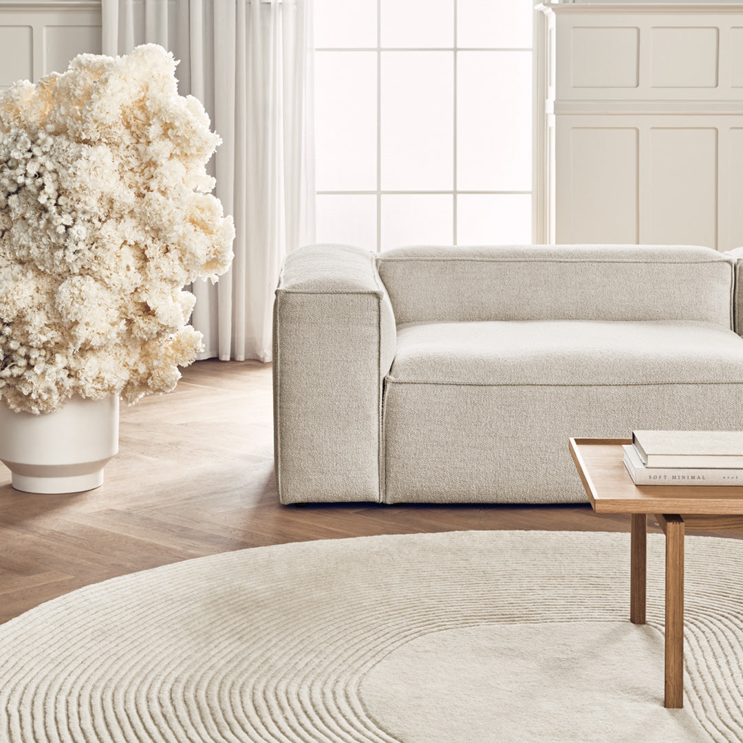 Textured light beige sofa with a soft cream round rug, complementing neutral decor and pastel floral arrangement.