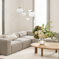 Beige sectional sofa with neutral tones, white pendant lights, and a vibrant floral arrangement on a light wood coffee table.