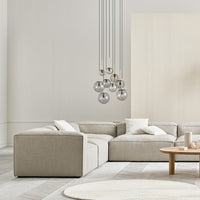 Beige sectional sofa with soft pillows, modern light fixtures, and a textured white rug in a minimalist living space.
