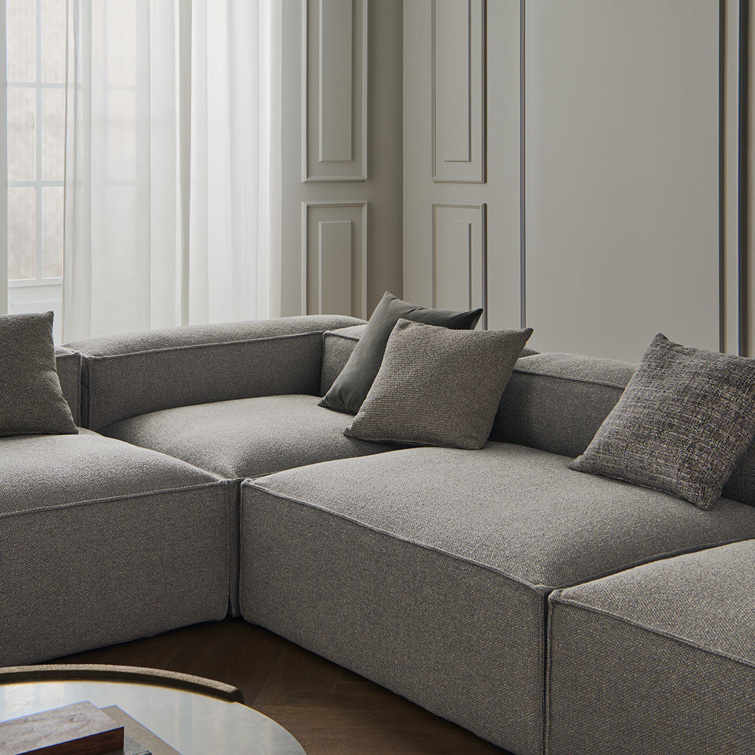 Gray sectional sofa with textured fabric and matching throw pillows, set against a neutral backdrop for a modern look.