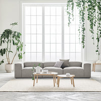 Modern grey sectional sofa in a bright, airy room with natural light and greenery, accented by neutral-toned rugs and decor.