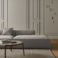 Gray sectional sofa with light gray accents, set against a minimalist backdrop and complemented by a textured rug.