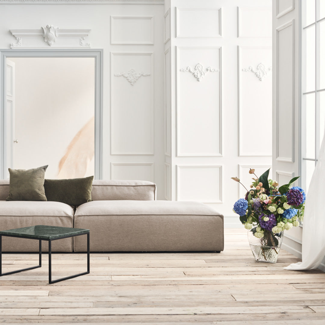 Beige sectional sofa with olive green and cream cushions, paired with a colorful floral arrangement in a bright, airy space.