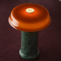 Orange glass lampshade on a green marble base, set against a deep burgundy background. Elegant modern design.