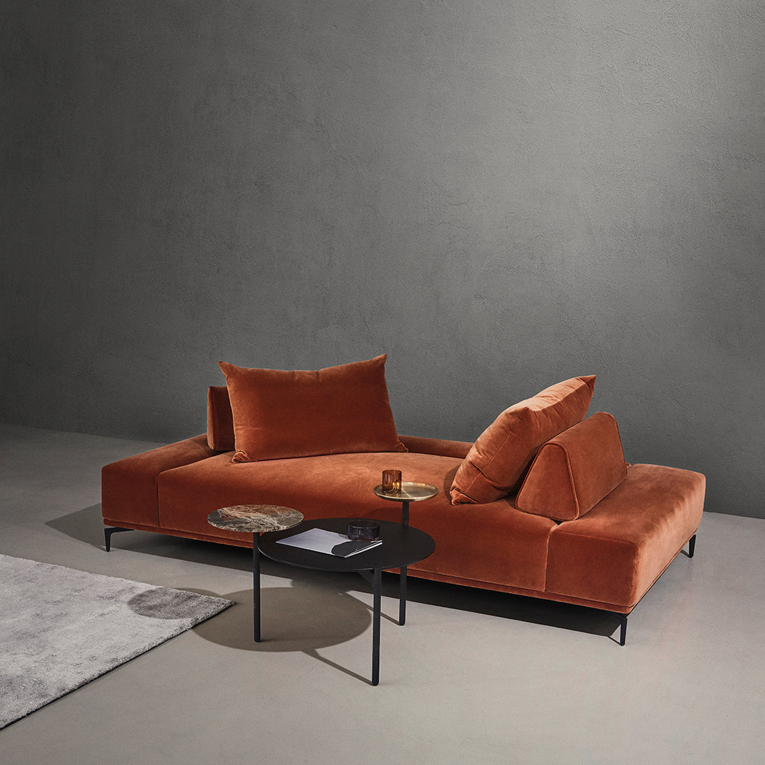 Rust orange velvet sofa with plush cushions, paired with a sleek black side table against a neutral backdrop.
