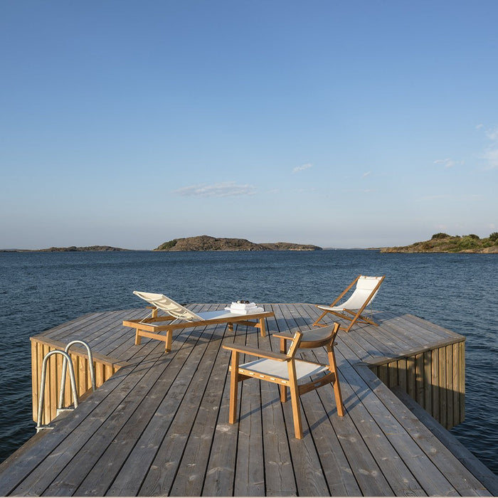 Wooden deck with grey planks, white canvas lounge chairs, and a serene blue water backdrop under a clear sky.