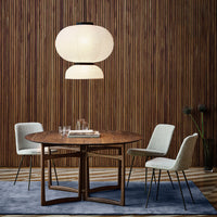 Round wooden table with beige chairs on a blue rug, complemented by a soft white pendant light and wooden backdrop.