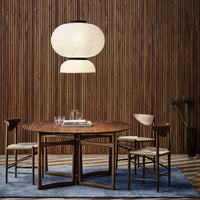 Round wooden dining table with beige chairs, soft blue rug, and textured wood backdrop. Elegant neutral tones and minimal patterns.