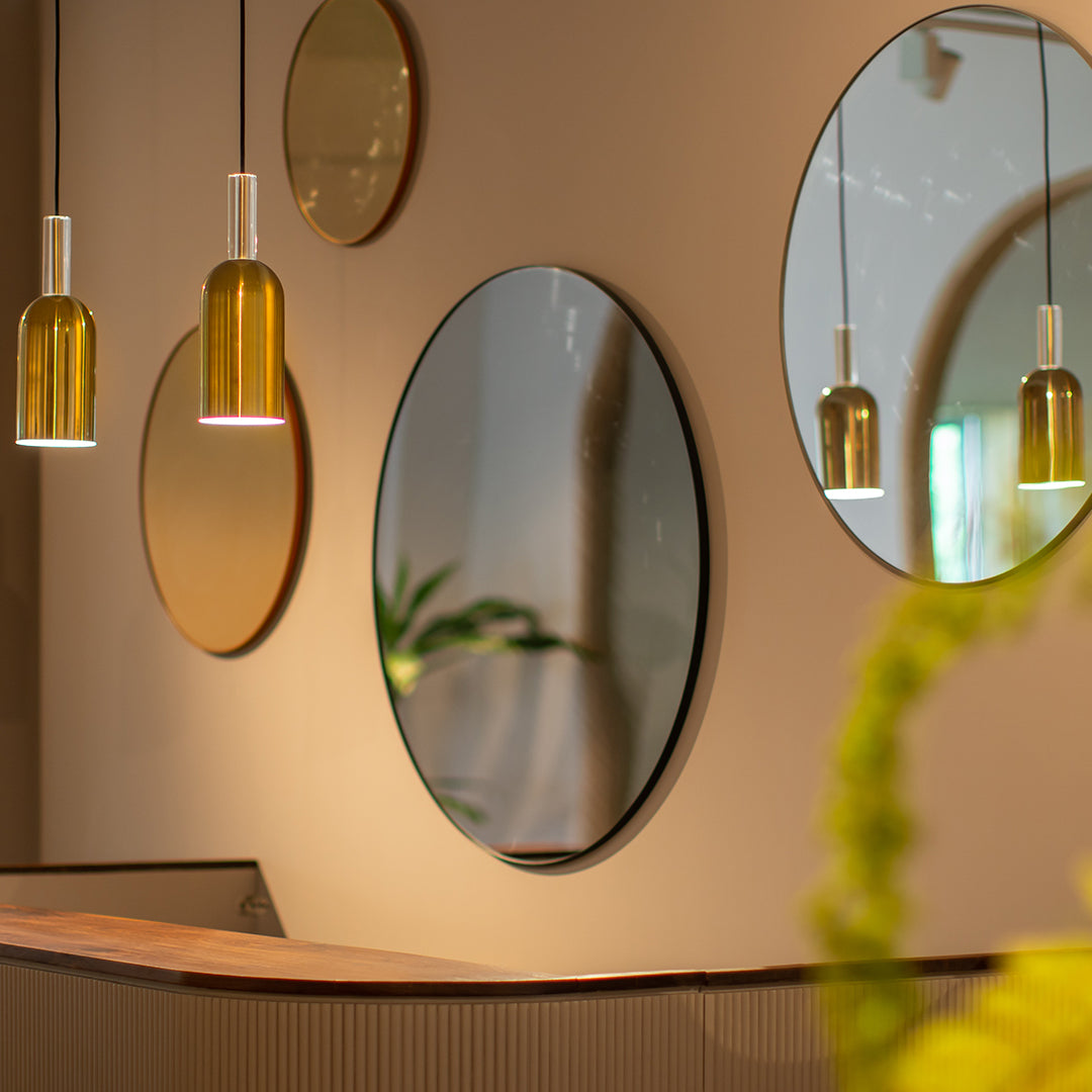 Round mirrors with gold accents and yellow pendant lights against a soft, neutral wall backdrop.