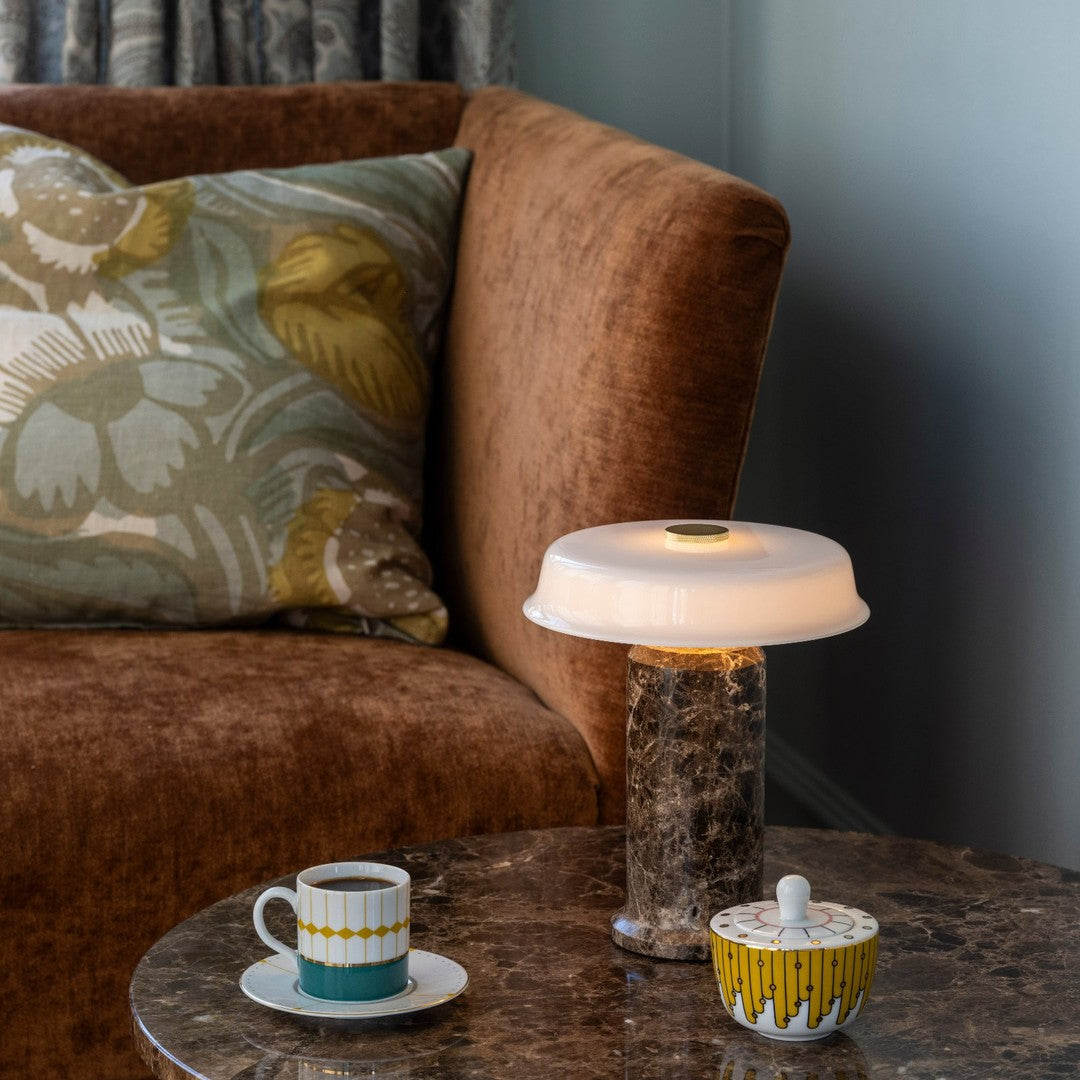 "Brown vintage couch, teal and yellow patterned accents, floral cushions, marble table with stylish lamp and cups."