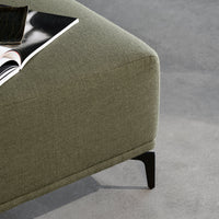 Green textured fabric ottoman with sleek black legs on a gray surface. Modern and stylish design elements.