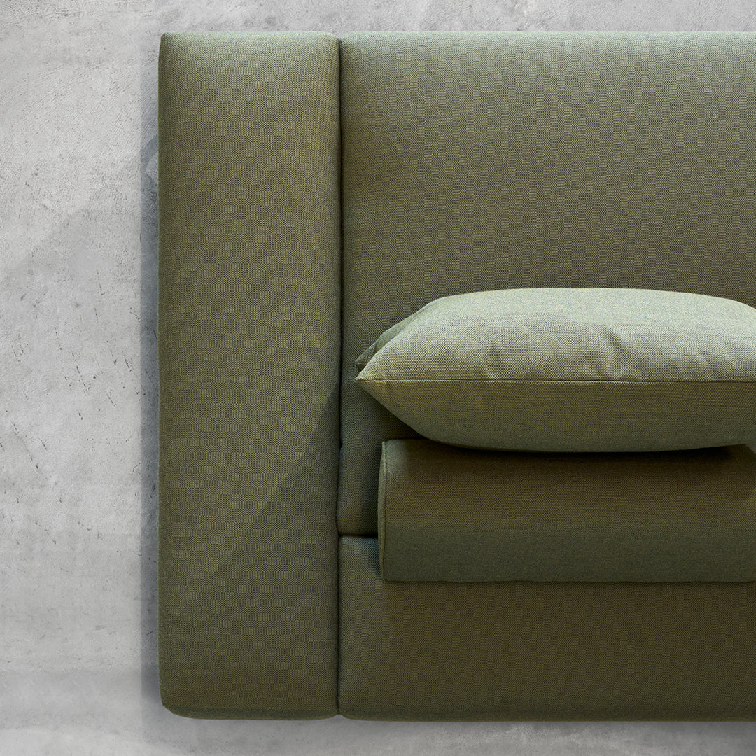 Olive green upholstered headboard with smooth, minimalistic design and matching accent pillow. Modern texture and style.