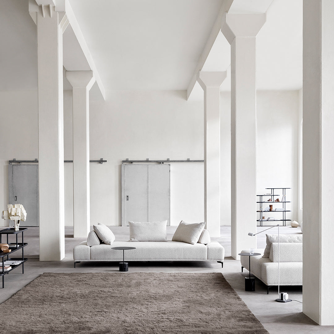 Modern living room with neutral tones, soft gray upholstery, and a textured brown rug, complemented by minimalist decor.