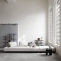 Modern white sectional sofa with soft textures, paired with black shelving and minimalist decor in a light, neutral space.