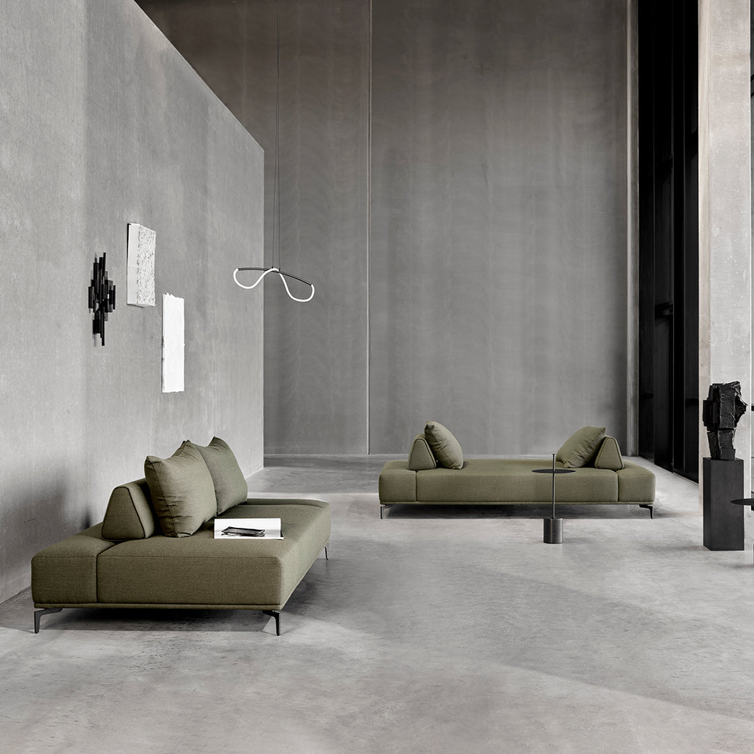 Sleek olive green sofas with modern design against a minimalist gray concrete backdrop.