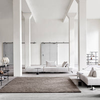 Neutral beige area rug on a light gray floor, with minimalist white and black furnishings for a modern aesthetic.
