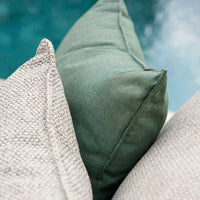 Green and textured gray decorative pillows layered together, complementing a serene outdoor setting.