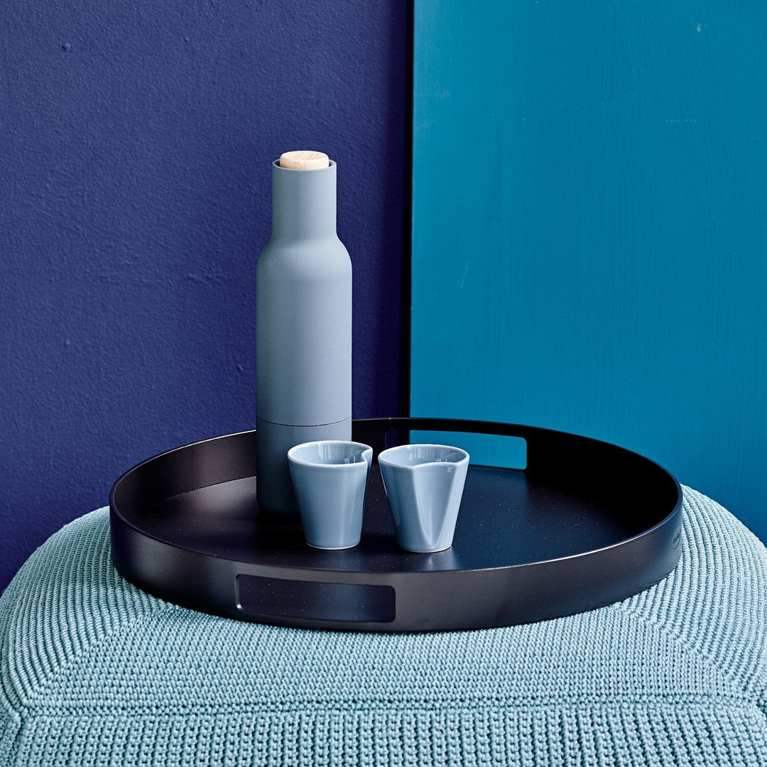 Blue and black dinnerware set featuring a matte tray, round base, and sleek bottles and cups against a textured backdrop.