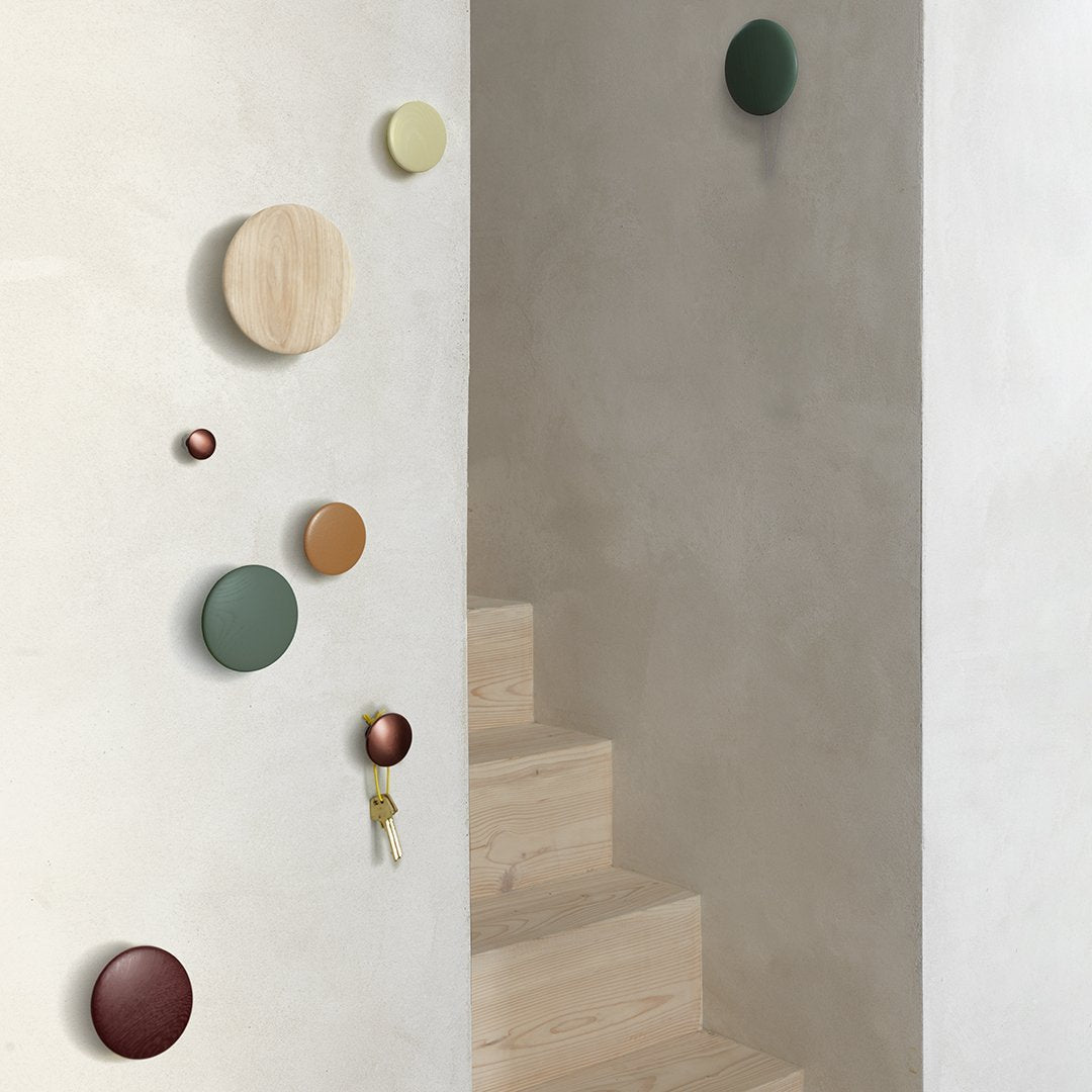 Colorful round wall hooks in shades of green, brown, yellow, and natural wood against a minimalist beige background.