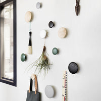 Colorful wall hooks featuring wood, black, white, green, and gray finishes in a modern, minimalist arrangement.