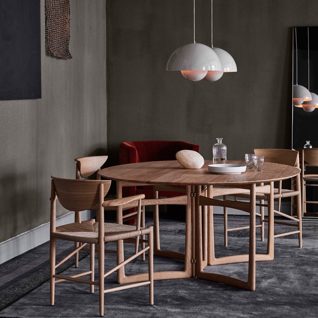 Modern round wooden dining table with natural grain, complemented by neutral-toned chairs and a dark gray rug.
