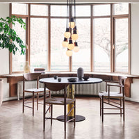 "Modern round black table with wooden chairs, surrounded by large windows and soft golden light accents."