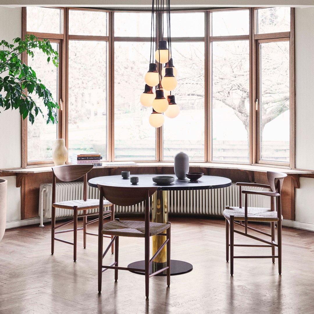 "Modern round black table with wooden chairs, surrounded by large windows and soft golden light accents."