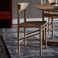 Natural wood chair with woven seat, featuring a light oak finish and minimalistic design against a textured gray background.