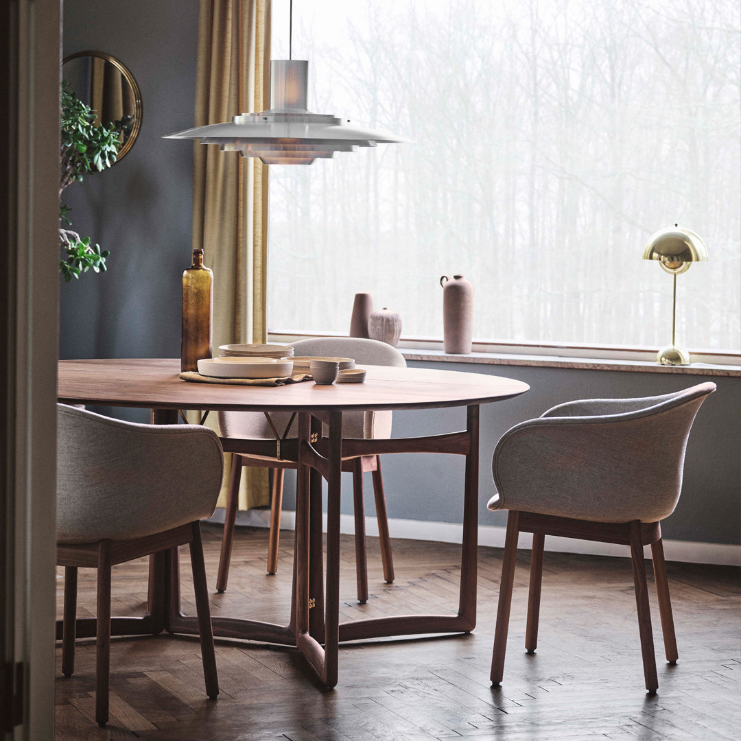 Modern dining room featuring a round wooden table and soft gray chairs, set against muted walls and natural light.