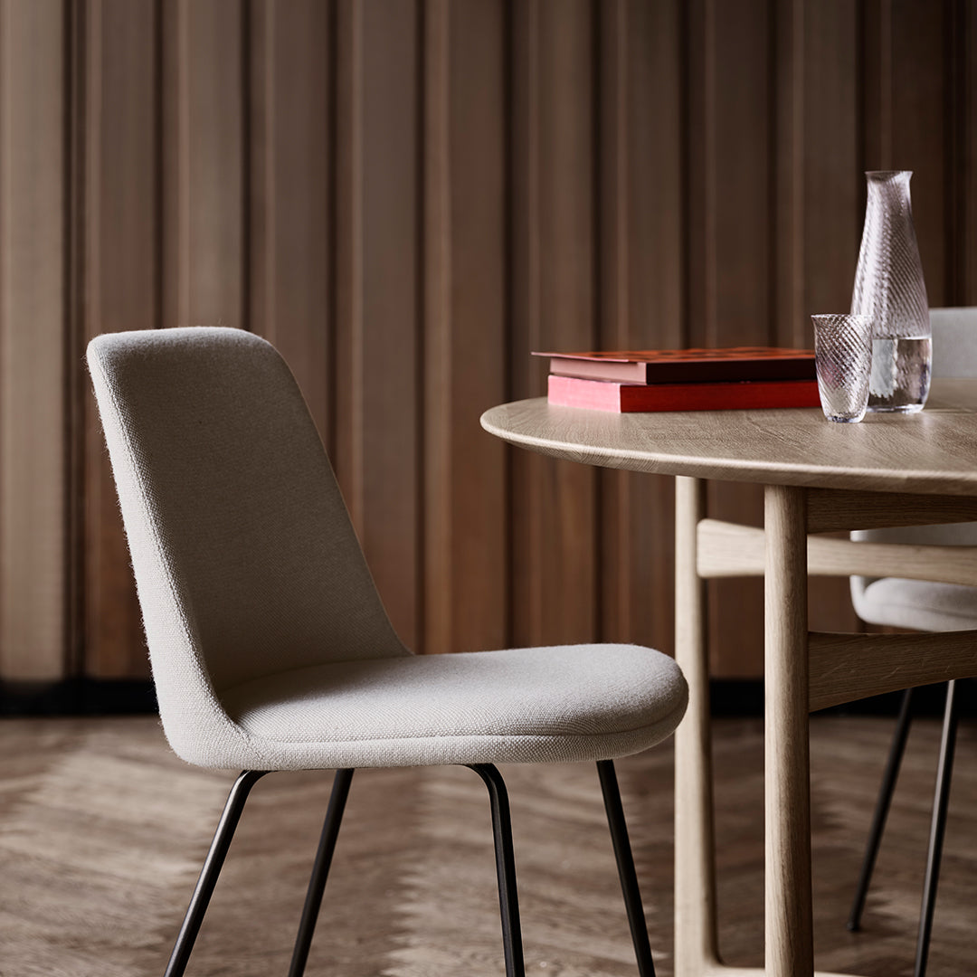 Light gray upholstered chair with sleek black legs, set against warm wooden paneling and a minimalist table setup.