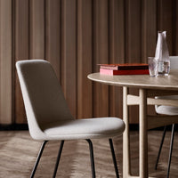 Light gray upholstered chair with sleek black legs, set against warm wooden paneling and a minimalist table setup.