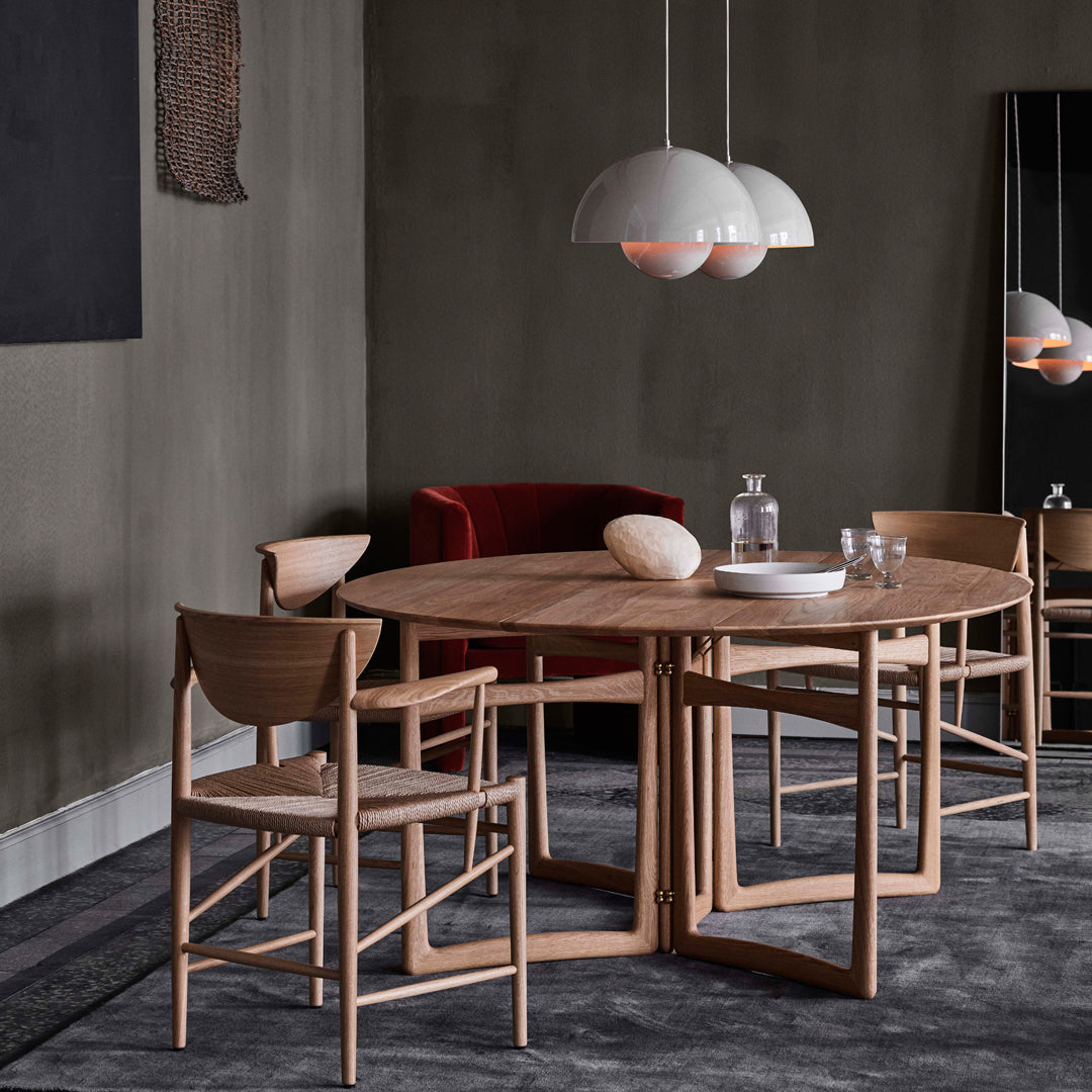 Natural wood dining table with beige chairs, complemented by a gray wall and deep red sofa, featuring modern pendant lights.