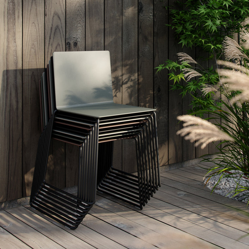 Stack of sleek gray chairs with black metal frames against a wood backdrop, complemented by green foliage.