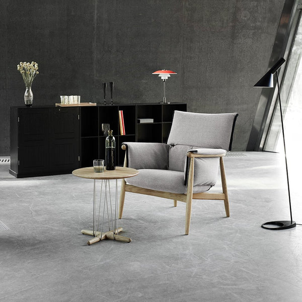 Gray upholstered armchair with light wood accents, paired with a round coffee table and minimalist decor.