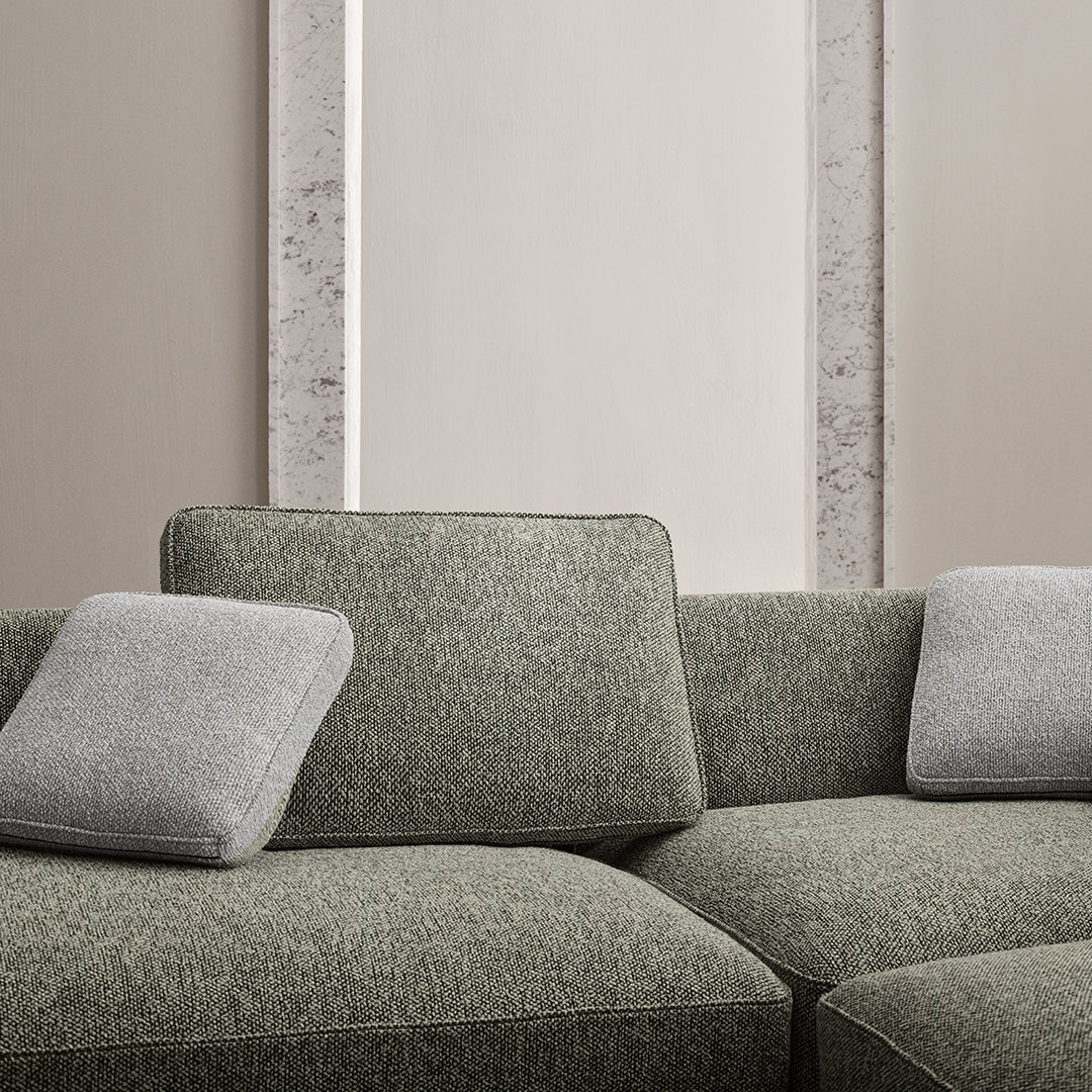 Textured green sofa with gray accent pillows, featuring a modern, minimalist pattern against a neutral backdrop.