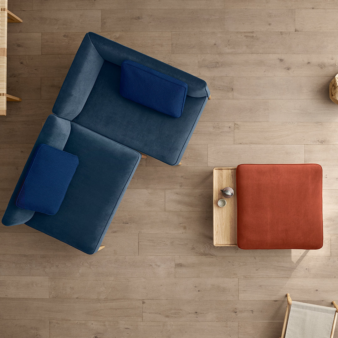 "Blue and navy sectional sofa with a rust-colored accent pillow and wooden coffee table on a light wood floor."